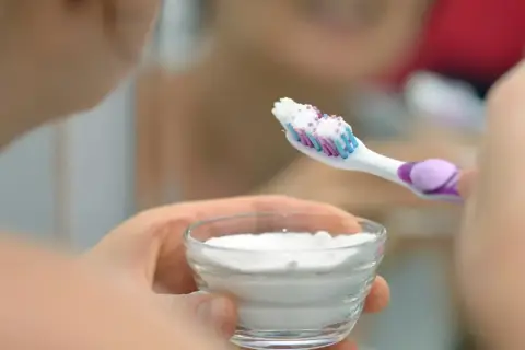 Mano tiene una spazzolino con dentifricio e una ciotola con polvere bianca, forse per sbiancare i denti con perossido di idrogeno.
